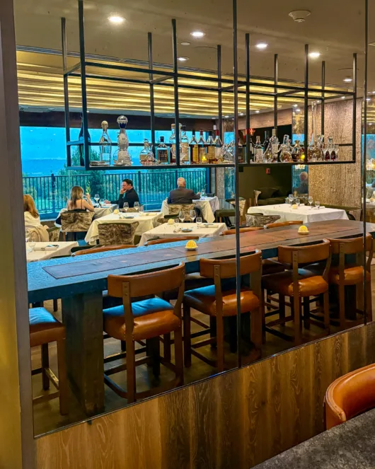 Long wooden table with leather chairs beneath suspended spirits shelving in Restaurant Latour’s dining room.