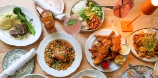 Overhead view of Coastal Canteen's seafood and American dining spread in Manasquan, New Jersey, featuring oysters, shrimp ceviche, scallop risotto, fish and chips, grilled salmon, steak, fresh salads, cocktails, and seasonal entrées