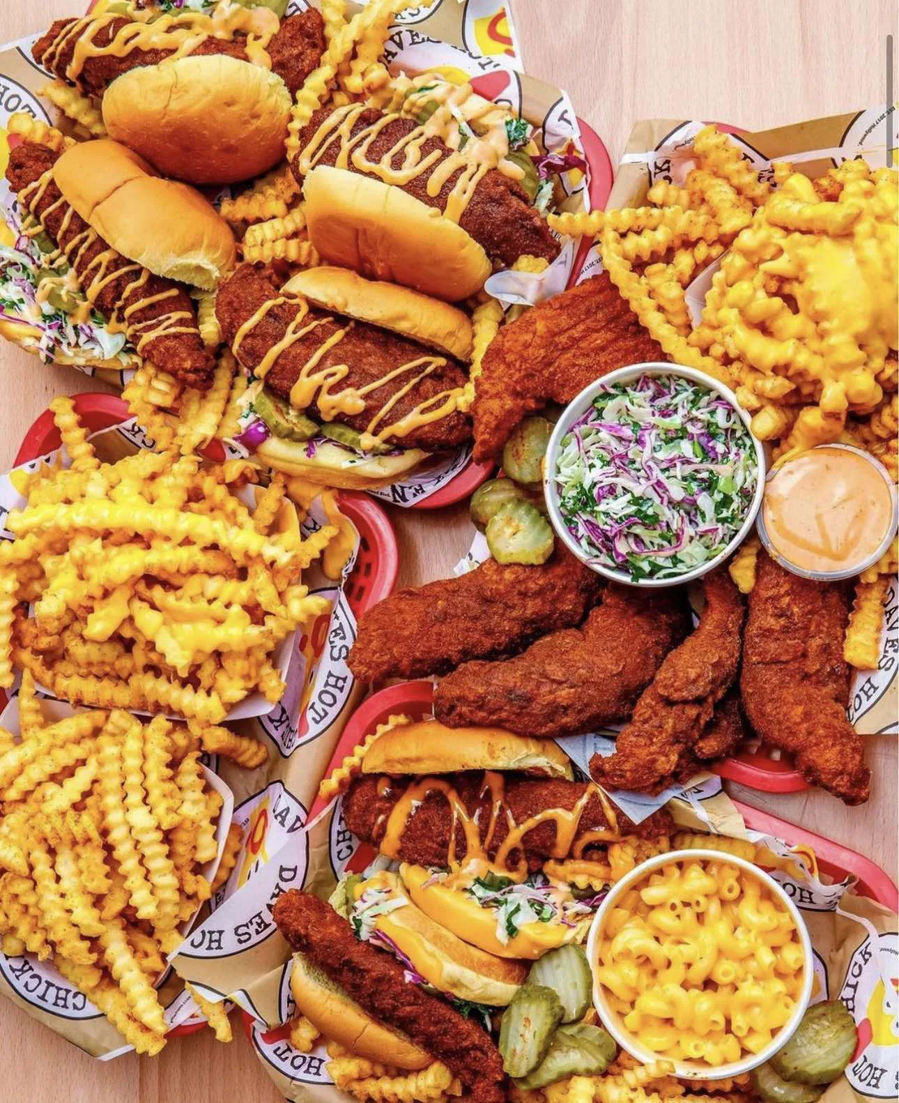 Assortment of crispy hot chicken sandwiches, tenders, crinkle-cut fries, coleslaw, pickles, and macaroni and cheese served on a table at Dave's Hot Chicken.
