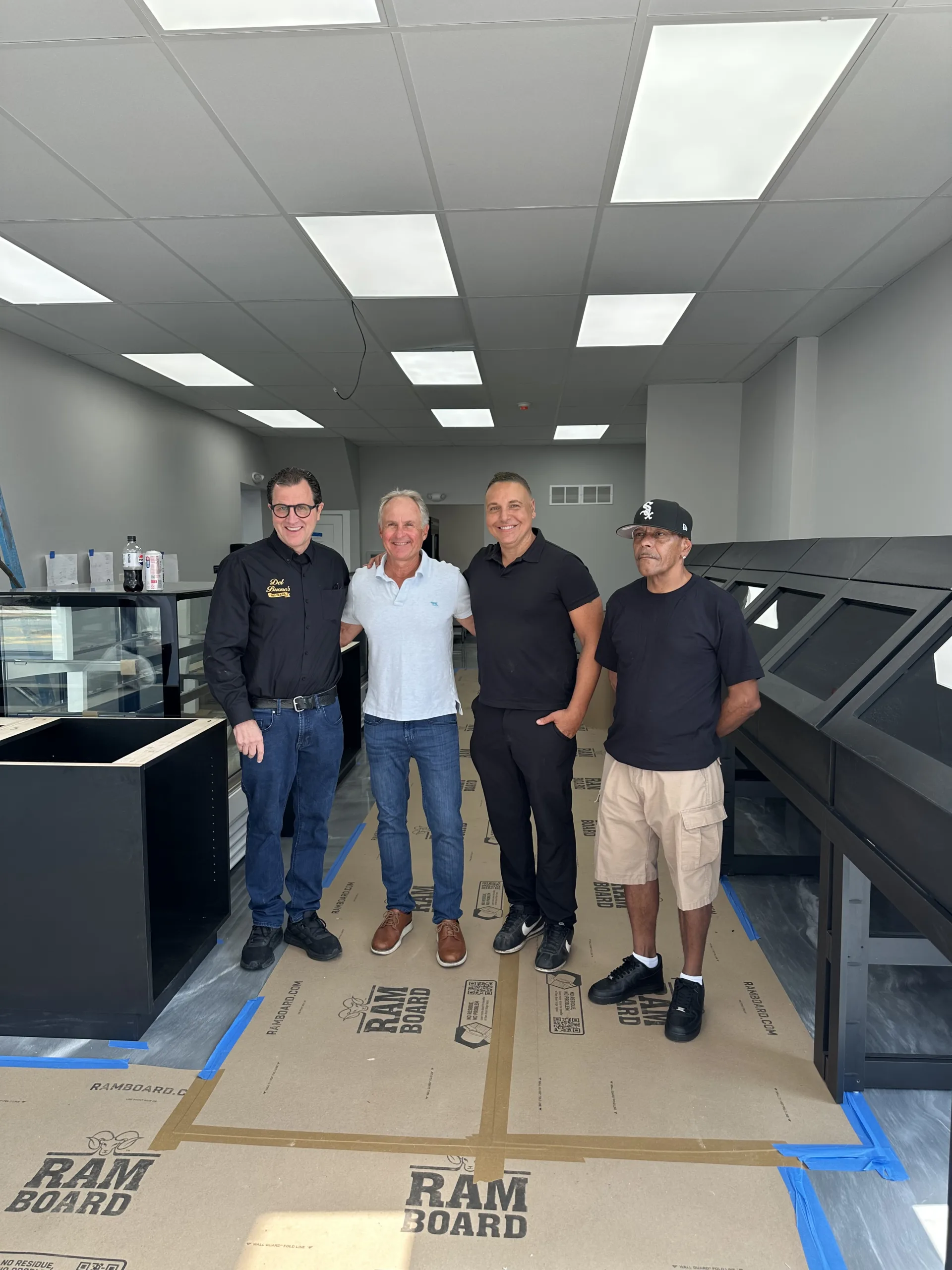 Four men standing together inside a restaurant under construction, posing for a photo near the service counter and display cases.