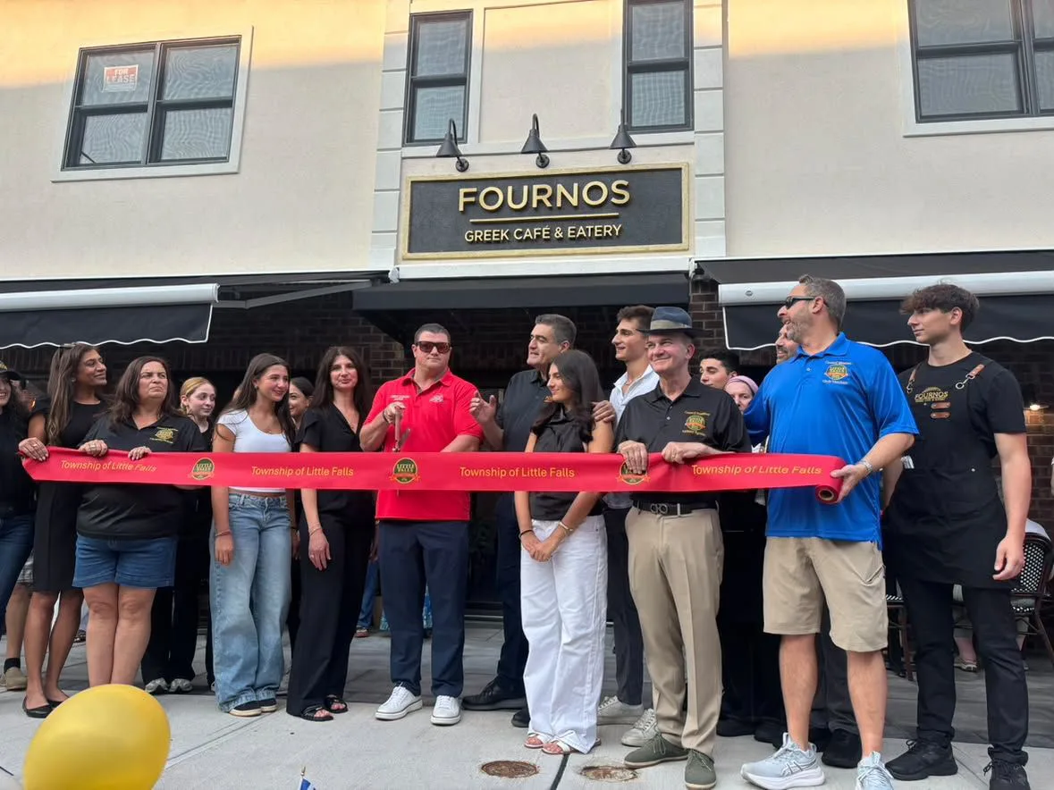 A group gathers outside Fourno’s Greek Café & Eatery for a ribbon-cutting ceremony, standing behind a red Township of Little Falls ribbon.