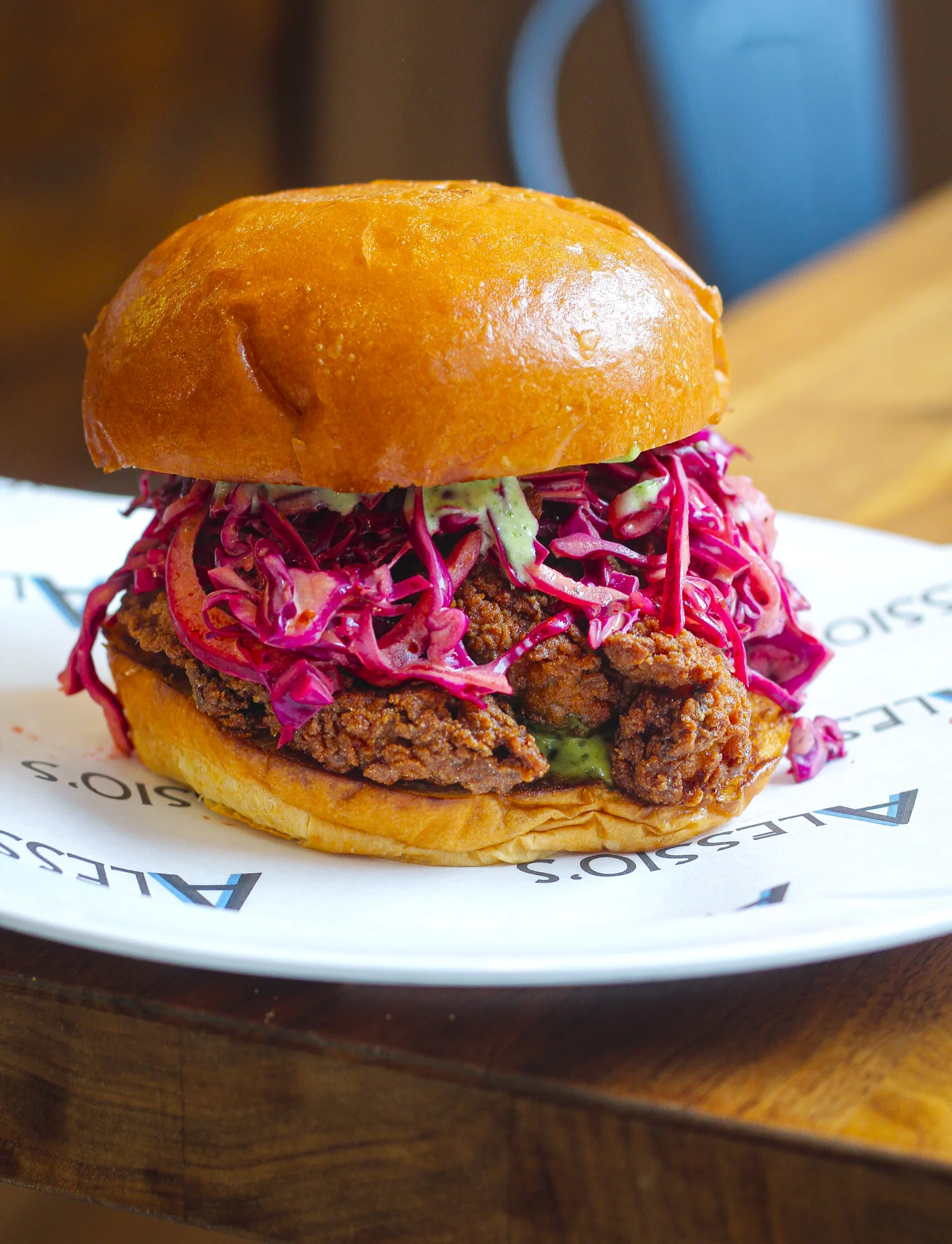 A crispy fried chicken sandwich topped with vibrant purple cabbage slaw and creamy green sauce on a toasted brioche bun.