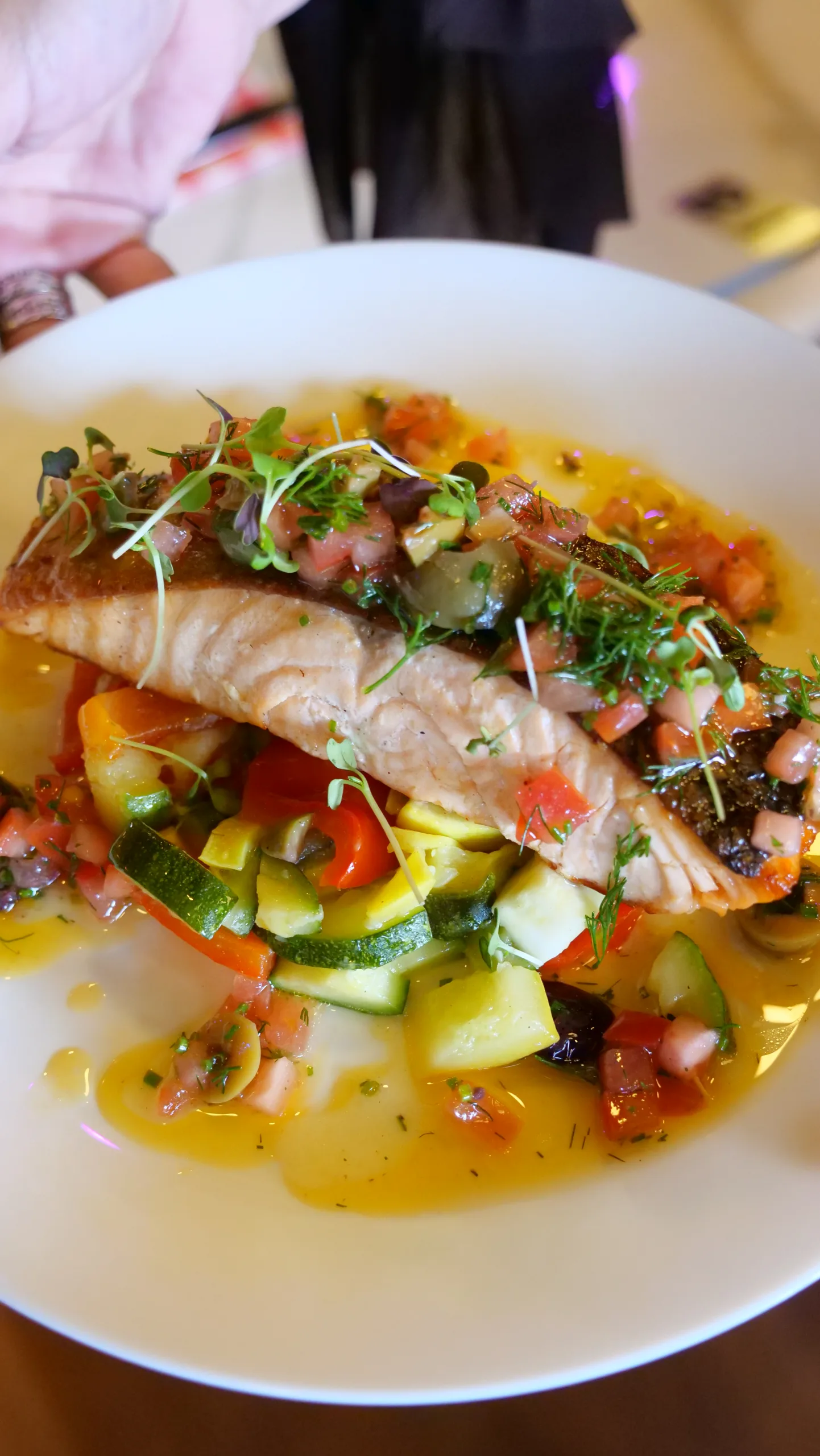 Pan-seared salmon topped with fresh herbs and diced vegetables, served over sautéed zucchini, peppers, and olives at Le Bistrot.
