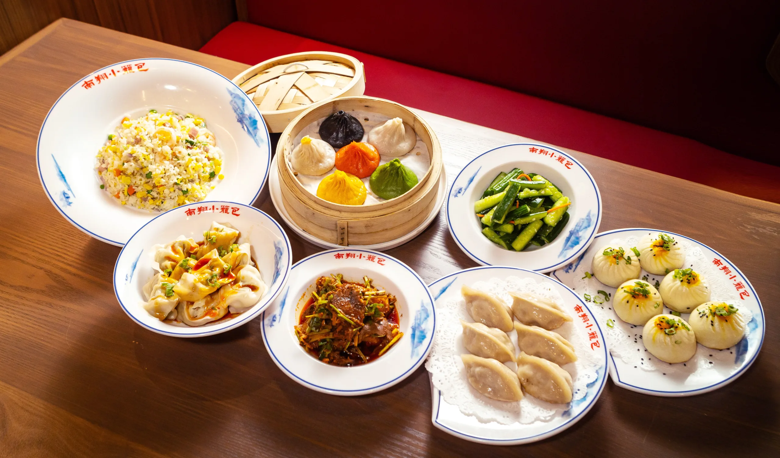Nan Xiang Xiao Long Bao spread featuring colorful soup dumplings, steamed buns, wontons, fried rice, and vegetable dishes.