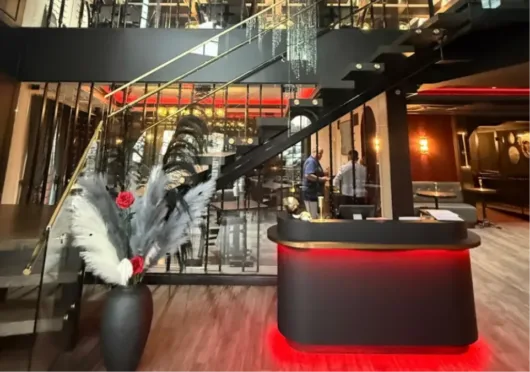 Interior of Sinner’s Seafood & Steakhouse in Kenilworth, NJ, featuring a modern staircase, crystal chandeliers, and a red-lit reception desk.