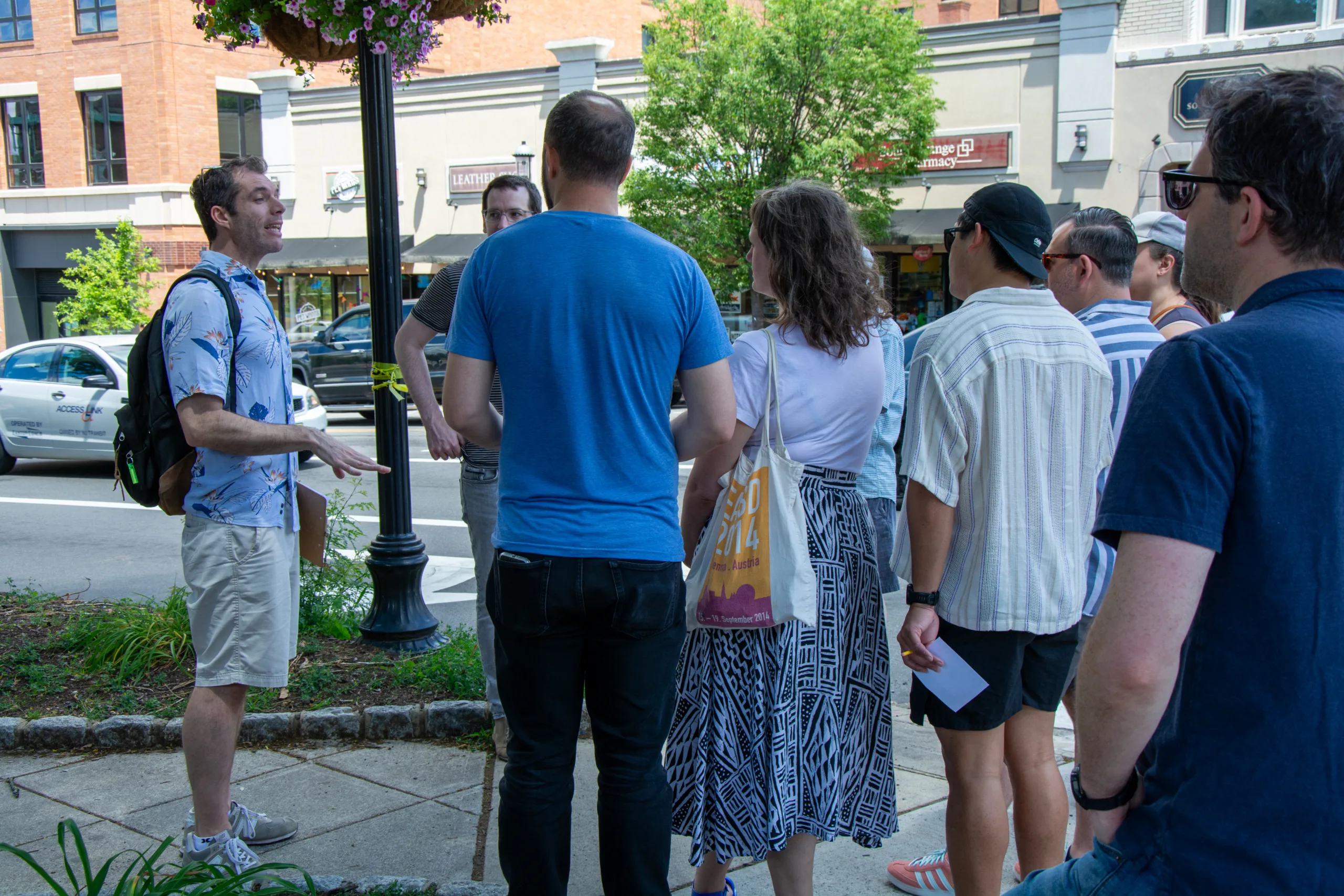 A tour guide speaks to a group of participants during a Chow Town food tour along a downtown sidewalk.